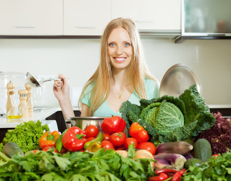 happy blonde woman cooking with  vegetables in kitchen
