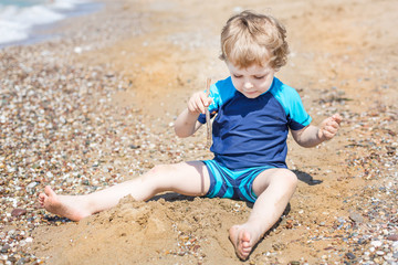 Little toddler boy playing with sand and stones on the beach