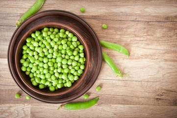 Green peas in a ceramic bowl on old wooden background