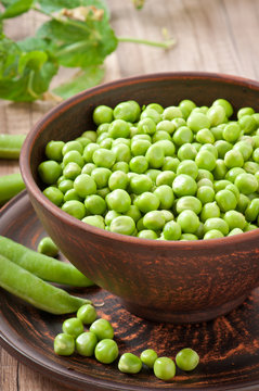 Green peas in a ceramic bowl on old wooden background