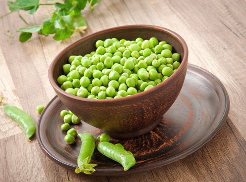 Green peas in a ceramic bowl on old wooden background