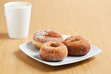 Three jam doughnuts on a white plate with a mug of coffee