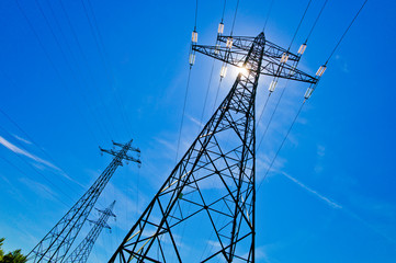 Strommast mit Sonne vor blauem Himmel