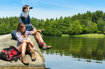 Teenage hikers birdwatching at lake - obrazy, fototapety, plakaty