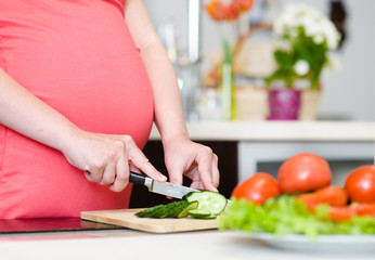 Obraz na płótnie Canvas Close up pregnant woman with knife on kitchen cuts cucumber