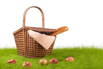 Picnic basket with long loaf and apples on the grass.
