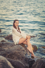 Fototapeta na wymiar Beautiful young woman sitting on the stone on the seashore