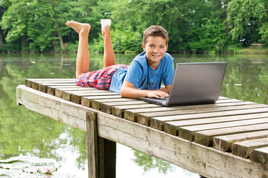 Freundlicher Jungendlicher mit Notebook am idyllischen Teich