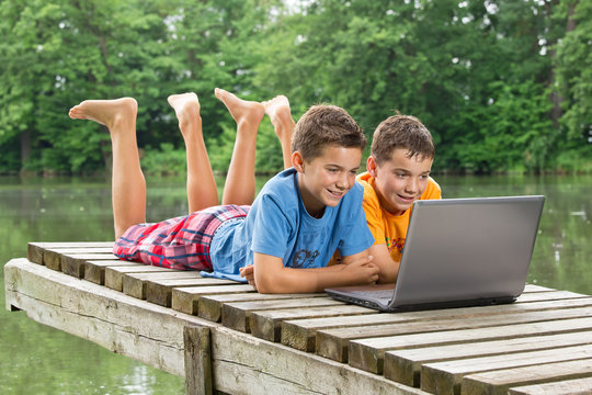 Zwei jungendliche Freunde mit Notebook am idyllischen Teich