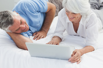 Obraz premium Cheerful couple using a laptop in bed