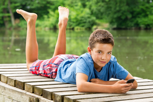 Freundlicher Jungendlicher mit Smartphone am idyllischen Teich
