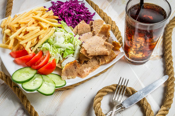 Closeup of vegetables, fries and meat kebab served with cold Cok