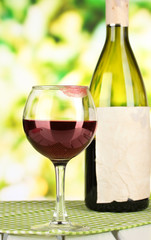 Glass of wine and bottle on table on nature background