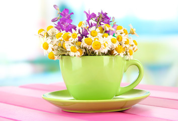 Bouquet of chamomile flowers in cup, on bright background