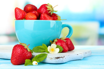 Ripe sweet strawberries in cup on blue wooden table