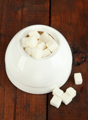 Refined sugar in white sugar bowl on wooden background
