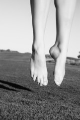 feet of jumping on green field woman