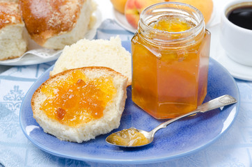 Sweet bun with apricot jam and coffee for breakfast, close-up