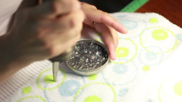 Woman sticking sequins on knitted fabric
