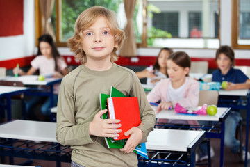Schoolboy Holding Books While Standing In Classroom