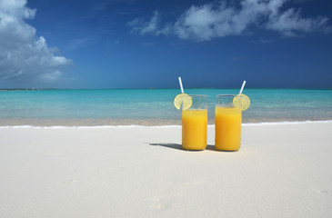 Two glasses of orange juice on the sandy beach