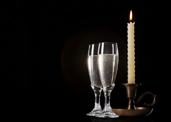 Two glasses of champagne and candle on black background