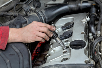 Car mechanic replacing ignition coil, gasoline engine