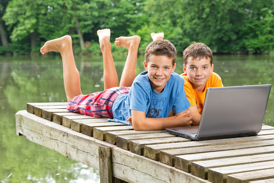 Zwei jugendliche Freunde mit Notebook am idyllischen Teich
