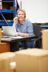 Fototapeta na wymiar Worker In Warehouse Wearing Headset And Using Laptop