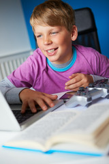 Fototapeta na wymiar Boy Studying In Bedroom Using Laptop