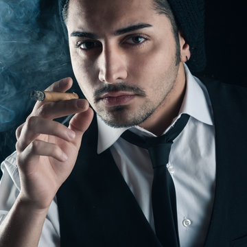 Young man close up portrait with cigar against dark background.