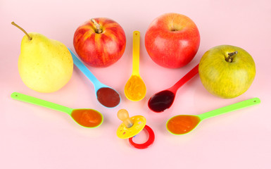 Baby puree in spoons with nipple and fruits on pink background