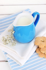 Blue jug with milk and cookies on wooden picnic table close-up
