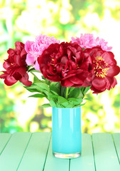 Beautiful peonies in vase on table on bright background