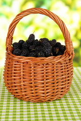 Fototapeta na wymiar Ripe mulberries in wicker basket on table on bright background