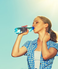 woman drinks water from a bottle in the summer outdoors on the s