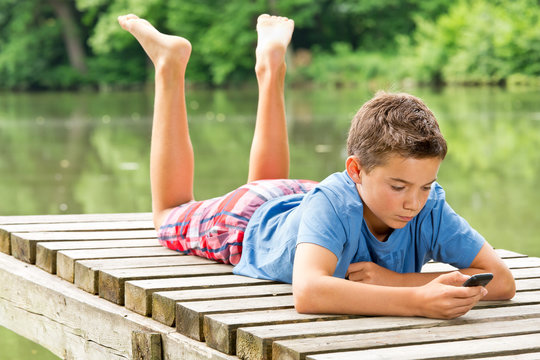 Jugendlicher / Kind mit Smartphone am idyllischen Teich