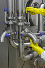 hands in yellow gloves on tap and lever of technological system