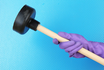 Toilet plunger in hand on blue background