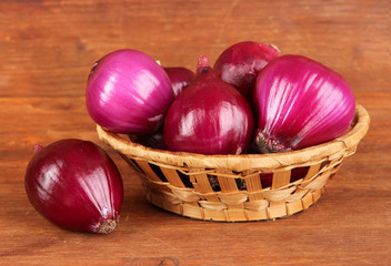 Purple onion in wicker basket on wooden background