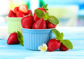 Ripe sweet strawberries in bowls on blue wooden table