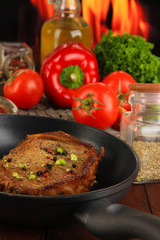 Piece of fried meat on pan on wooden table on fire background