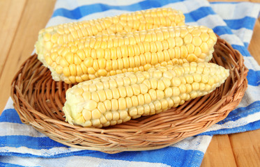 Fresh corn on wicker mat, on wooden background