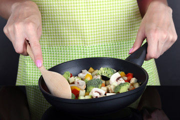 Hands cooking vegetable ragout in pan on gray background