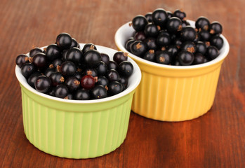 Fresh black currant in bowls on wooden background