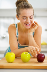 Happy young woman choosing between two green and one red apple