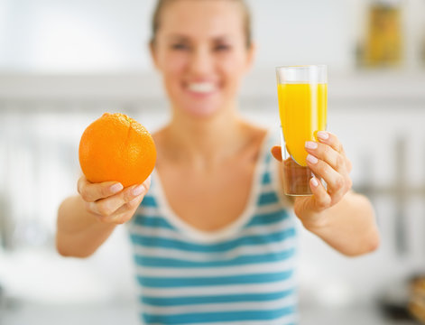 Closeup on glass of orange juice and orange in hand of woman