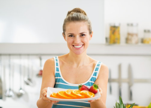 Happy young woman holding plate with strawberry and orange