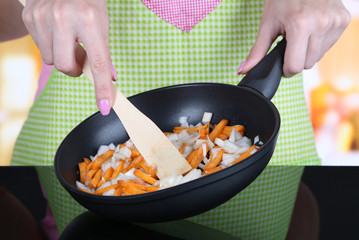 Hands cooking fried onion with carrot in pan in kitchen