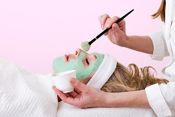 Beautician brushing green facial mask on a woman. - obrazy, fototapety, plakaty